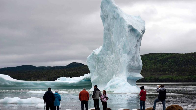 Tourists look at an icebergs from the seashore of King's Point on July 3, 2019 in Newfoundland, Canada. Formerly the center of cod fishing, the island province now sees more and more Icebergs that made their last trip from Greenland to Newfoundland. - The abundance of icebergs, which continue to venture further into Canadian waters, has created a new form of tourism, iceberg sightseeing. In 2018, more than 500,000 tourists visited the province of Newfoundland, contributing nearly 570 million Canadian dollars (389 million euros) to the local economy, according to the estimates of the provincial government. (Photo by Johannes EISELE / AFP)