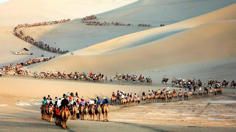 This photo taken on August 10, 2019 shows tourists riding camels in the desert in Dunhuang in China's northwestern Gansu province. (Photo by STR / AFP) / China OUT