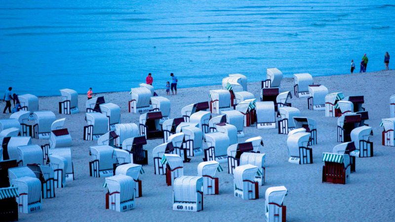 Holiday makers walk past beach chairs along the Baltic Sea beach in Sellin near Binz and Baabe on the island of Ruegen, northeastern Germany, as night falls on August 18, 2019. (Photo by Jens Büttner / dpa / AFP) / Germany OUT