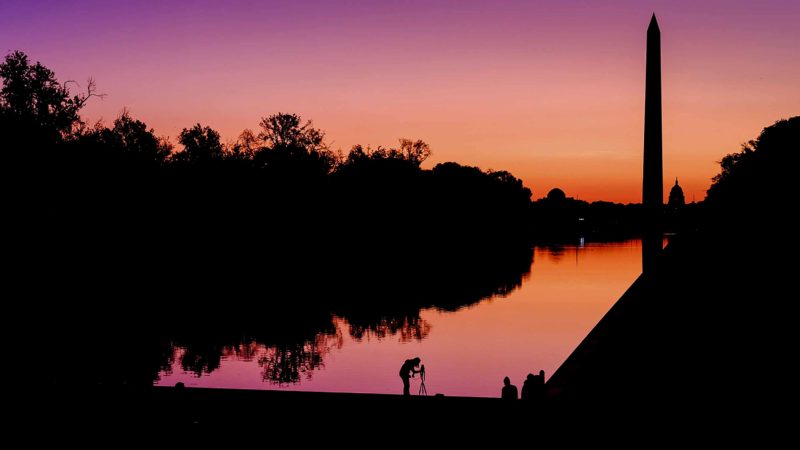 A photographer lines up her shot at the National Mall reflecting pool as the sun begins to rise behind the Washington Monument and the U.S. Capitol building in Washington, Saturday, Sept. 21, 2019. (AP Photo/J. David Ake)