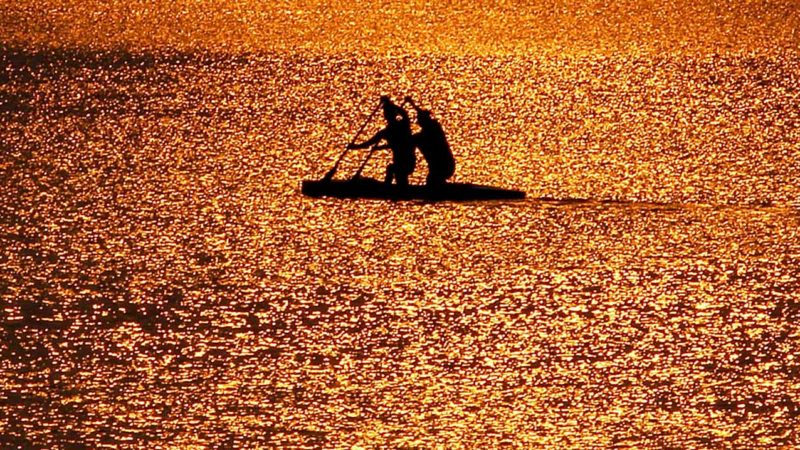 TOPSHOT - Row-men with their boat are silhouetted in the waters of Sukhna Lake during sunrise in Chandigarh on September 22, 2019. (Photo by Vijay MATHUR / AFP)