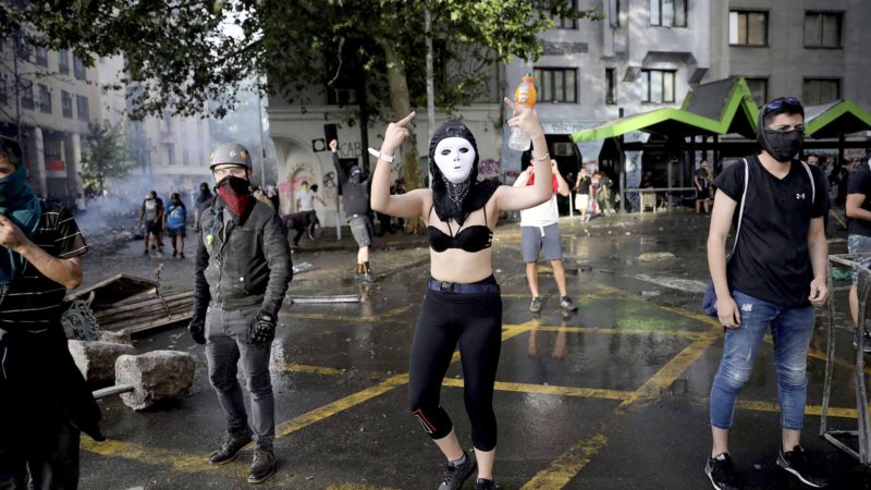EDS NOTE: OBSCENITY - A masked demonstrator gestures during an anti-government march in Santiago, Chile, Tuesday, Oct. 22, 2019. Unrest began last week when a rise in subway fares led to student protests, but then spread nationwide, fueled by frustration among many Chileans who feel they have note shared in the economic advances in one of Latin America’s wealthiest nations. (AP Photo/Rodrigo Abd)
