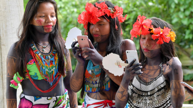 Embera indigenous child check their mobile phones during the preparation of a giant "patacon" -fried flattened pieces of green plantains- in Ipeti Embera, Chepo Distric, Panama, on October 16, 2019. - The Embera indigenous community of Panama managed to cook the largest patacon in the world, which entered the Guinness World Records. Photo/RSS