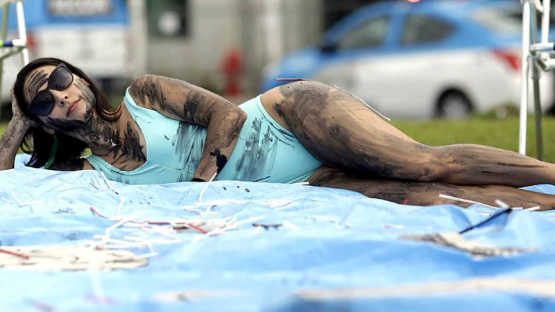 In this Oct. 10, 2019 photo, a demonstrator painted with fake oil lies on a tarp during a protest against the auction for the exploration of oil fields close to Abrolhos, a marine national park in Bahia state, in front of the Grand Hyatt Hotel where the auction is taking place in Rio de Janeiro, Brazil. Under pressure from environmental organizations, none of the 17 companies involved in the process presented any offers. (AP Photo/Silvia Izquierdo)