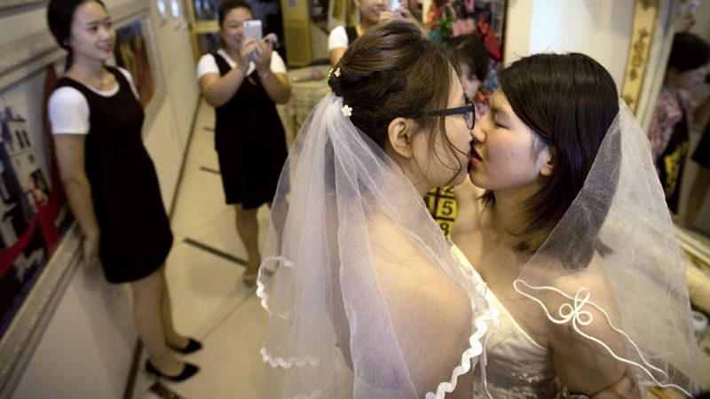 FILE - In this July 2, 2015, file photo, Teresa Xu, left, and Li Tingting, right, share a kiss as clerks take photographs in a beauty salon where the two were preparing for their wedding in Beijing. LGBT activists in China are seeking to legalize same-sex marriage through a novel tactic: submitting opinions on a draft new civil code to the country’s legislature. (AP Photo/Mark Schiefelbein, File)