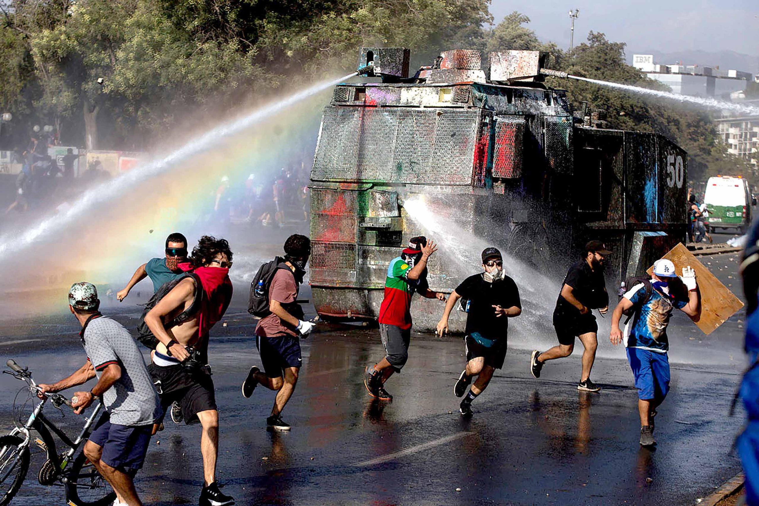 Demonstrators run as a riot police vehicle sprays water during a protest against Chilean President Sebastian Pinera's government in Santiago, on January 10, 2020. - Chile has been rocked by months of protests that began with strikes over metro fare hikes and quickly escalated into the most severe outbreak of social unrest since the end of the dictatorship of Augusto Pinochet nearly 30 years ago. (Photo by CLAUDIO REYES / AFP)