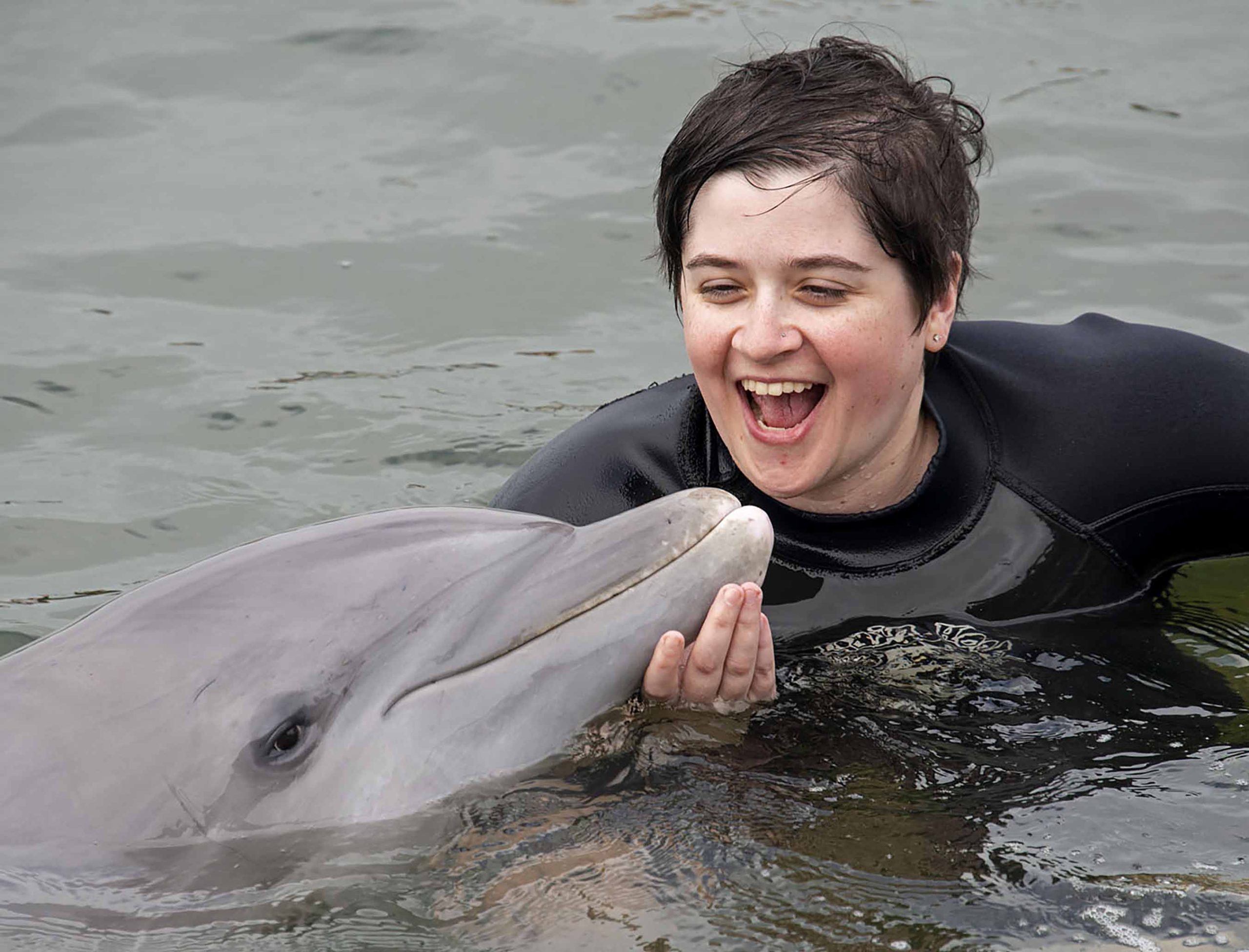 In this photo provided by the Florida Keys News Bureau, retired U.S. Army medic Rachael Rodgers reacts after kissing Santini the dolphin Friday, Jan. 10, 2020, at Dolphin Research Center in Marathon, Fla. Rodgers, who had her left leg amputated below the knee, and 42 other wounded military veterans interacted with dolphins as a facet of the Florida Keys Soldier Ride, a trip through the Florida Keys to Key West, Fla., riding adaptive bicycles down some segments of the Keys Overseas Highway. The event, that ends Sunday, Jan. 12, is organized by the Wounded Warrior Project. (Andy Newman/Florida Keys News Bureau via AP)