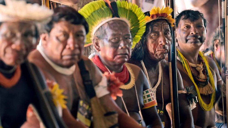 Indigenous tribesmen listen to their leader Cacique Raoni Metuktire (out of frame) of the Kayapo tribe,  during a press conference in Piaracu village, near Sao Jose do Xingu, Mato Grosso state, Brazil, on January 15, 2020. - Brazil's government will propose legalizing oil and gas exploration as well as hydroelectric dam construction on indigenous land, a report said Saturday, citing a draft of a bill to be sent to Congress. (Photo by CARL DE SOUZA / AFP)
