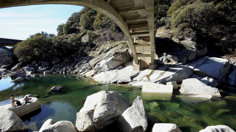 People rest on a rock along the South Yuba River meandering under the historic Highway 49 bridge in Nevada City, Calif., Tuesday, Feb. 11, 2020. (Elias Funez/The Union via AP)