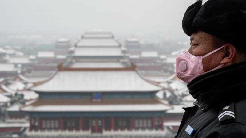 A security guard wears a protective mask to prevent the spread of the SARS-like virus as he looks out from the Jingshan park overlooking the Forbidden city (C) after a snowfall in Beijing on February 2, 2020. - A virus similar to the SARS pathogen has killed more than 300 people in China and spread around the world since emerging in a market in the central Chinese city of Wuhan. (Photo by NICOLAS ASFOURI / AFP)