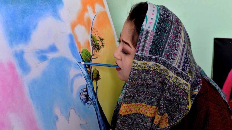 This photo taken on December 5, 2019 shows 19-year-old Afghan artist Robaba Mohammadi painting in her studio in Kabul. - Unable to use her hands, arms, or legs, Afghan artist Robaba Mohammadi has defied unlikely odds in a country that routinely discriminates against women and disabled people. Denied access to school, as a child she taught herself to paint by holding a brush in her mouth, clenching it between her teeth to create elaborate and colourful portraits. (Photo by NOORULLAH SHIRZADA / AFP) / TO GO WITH Afghanistan-disabilities-woman-social,FOCUS by Mushtaq MOJADDIDI