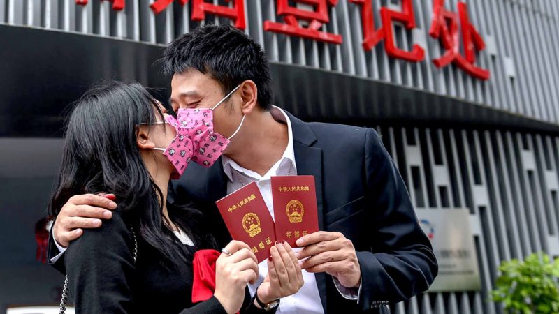 (200215) -- SHENZHEN, Feb. 15, 2020 (Xinhua) -- Deng Lingling (L) and Deng Junwei kiss while displaying their marriage certificates in front of the marriage registration office of the Civil Affairs Bureau of Nanshan District in Shenzhen, south China's Guangdong Province, Feb. 14, 2020. During the fight against the novel coronavirus epidemic, the Civil Affairs Bureau in Shenzhen has adopted the appointment system and cancelled the certification ceremony. Some procedures, including filling up application materials, have been transferred to the outdoor to avoid contact. (Xinhua/Mao Siqian)