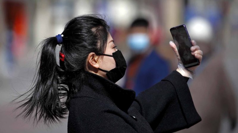 A masked woman wearing a hand glove takes a selfie at the Wangfujing shopping district in Beijing, Tuesday, March 10, 2020. For most people, the new coronavirus causes only mild or moderate symptoms, such as fever and cough. For some, especially older adults and people with existing health problems, it can cause more severe illness, including pneumonia. (AP Photo/Andy Wong)