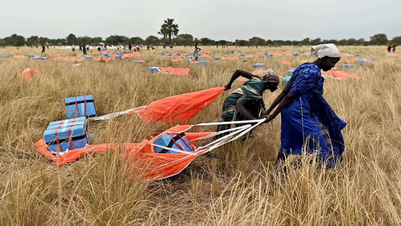 Villagers collect rations parachuted from a plane onto a drop zone at a village in Ayod county, South Sudan, where World Food Programme (WFP) have just carried out an food drop of grain and supplementary aid on February 6, 2020. - The villagers hear the distant roar of jet engines before a cargo plane makes a deafening pass over Mogok, dropping sacks of grain from its hold to the marooned dust bowl below. South Sudan is the last place on earth where food is airdropped, and in Mogok there was little other choice: without the tonnes of grains and cereals, people would have simply perished. (Photo by TONY KARUMBA / AFP)