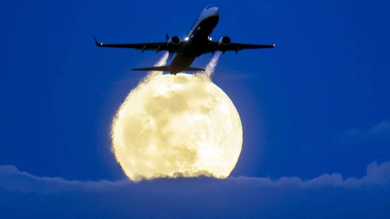 An aircraft passes the rising full moon breaking through the clouds at the airport in Frankfurt, Germany, Monday, March 9, 2020. (AP Photo/Michael Probst)