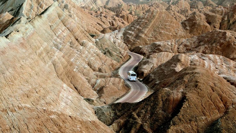 (200325) -- ZHANGYE, March 25, 2020 (Xinhua) -- Aerial photo taken on March 24, 2020 shows a tourist bus at the Danxia National Geological Park in Zhangye, northwest China's Gansu Province. Boasting a unique type of geomorphology formed from red-colored sandstones and characterized by steep cliffs, the Danxia National Geological Park reopened to the public under strict measures to fight against the COVID-19. (Xinhua/Zhang Zhimin)