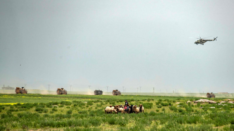 TOPSHOT - A woman tends to a flock of sheep, as a Russian air force Mil Mi-17 military helicopter flies over a joint Turkish-Russian military patrol in the countryside of the Syrian town of Darbasiyah near the Turkish border in the northeastern province of Hasakah, on April 22, 2020. (Photo by DELIL SOULEIMAN / AFP)