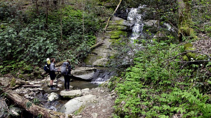 In this March 30, 2020, photo, Alexandra Eagle, right, and Jonathan Hall stand in front of a waterfall on the Appalachian Trail in Cosby, Tenn. The couple planned the to hike from Georgia to Maryland until coronavirus concerns forced them off the trail. (AP Photo/Sarah Blake Morgan)
