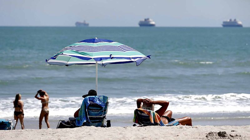 Despite a stay at home policy due to the coronavirus in Florida, beach goers enjoy the sun as cruise ships, without passengers, float offshore Saturday, April 4, 2020, in Cape Canaveral, Fla. Although some of the county beaches remained open, with out parking, many beach goers remained at home. (AP Photo/John Raoux)