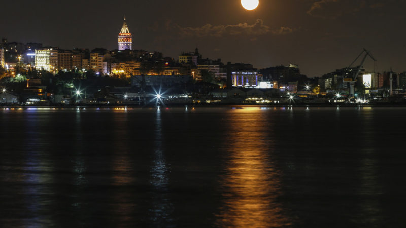 The moon rises behind Istanbul's skyline with the iconic Galata Tower, Friday, May 8, 2020, reflected on the Golden Horn, a few hours before the start of a two-day curfew declared by the government in an attempt to control the spread of coronavirus. The full moon, also known as the supermoon or Flower Moon, was visible on Thursday, May 7. (AP Photo/RSS)