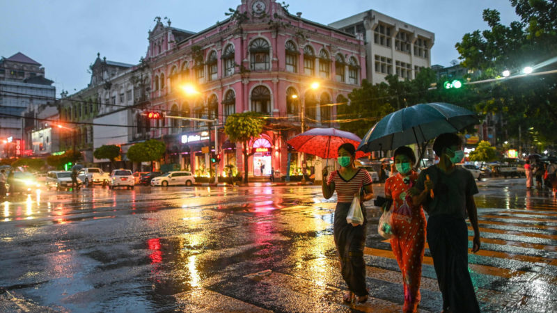 This photo taken on June 14, 2020 shows people holding umbrellas as they cross a road during rainfall in Yangon. (Photo by Ye Aung THU / AFP)