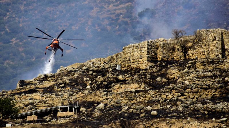 A firefighting helicopter drops water to extinguish flames during a wildfire  near the archaeological site of Mycenae in the northeastern Peloponnese, on August 30, 2020. - A wildfire broke out near the ruins of the Bronze Age stronghold of Mycenae in Greece on August 30, prompting the evacuation of visitors to the archeological site. (Photo by - / Eurokinissi / AFP)