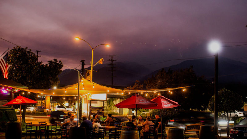 People dine at tables set up in the parking lot of a restaurant as smoke rises from the Bobcat Fire burning in the San Gabriel mountains in the distance, in Monrovia, California on September 16, 2020. - California faces more devastation from wildfires that have ravaged the West Coast, authorities warned on September 16, with strong winds and dry heat expected to whip up flames from dozens of blazes raging across the state. (Photo / RSS)