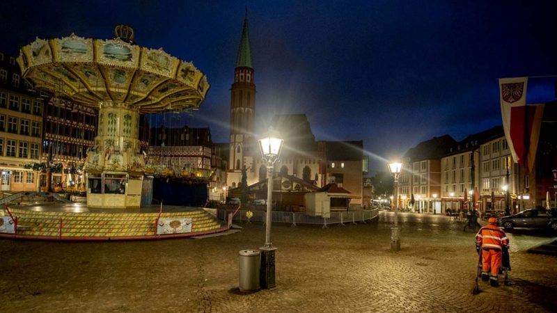 A public employee cleans the tourist hotspot Roemerberg square in Frankfurt, Germany, Wednesday, Oct. 7, 2020. The chain carousel, left, is part of the "autumn market" which should open on Thursday but the opening will be delayed due to the new restrictions to avoid the further outspread of the Coronavirus. (AP Photo/Michael Probst)