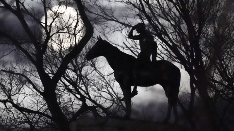 The full moon rises beyond a statue of a Native American scout on a bluff overlooking downtown Kansas City, Mo., Sunday, Nov. 29, 2020. (AP Photo/Charlie Riedel)