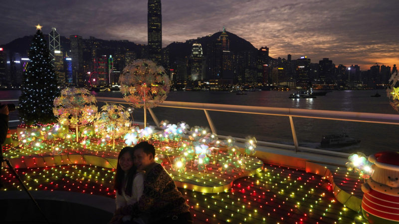 People take off their protective masks to take photographs of Christmas tree and holiday decorations in Hong Kong, Monday, Dec. 21, 2020. Hong Kong banned all flights from Britain on Monday, after a new and highly-contagious strain of the coronavirus swept through parts of southern England. (AP Photo/Kin Cheung)