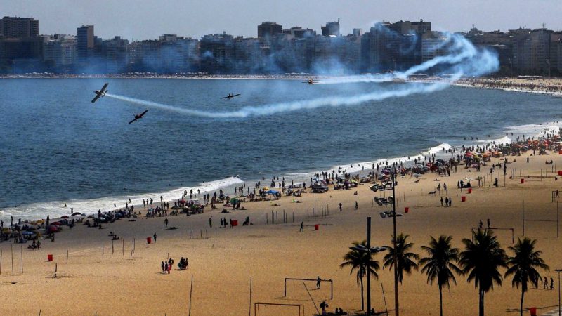 Stunt airplanes perform aerial maneuvers leaving smoke trails and entertaining beachgoers above Copacabana beach, Rio de Janeiro, Brazil, on December 31, 2020. - Rio de Janeiro's annual New Year's Eve beach bash and elaborate firework displays was cancelled due to the raging coronavirus pandemic. The city authorities will block beach access tonight, including a ban on vehicles along some 30 kilometres of Rio's coastline to prevent gatherings. (Photo by Carl DE SOUZA / AFP)