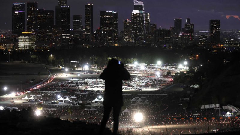 LOS ANGELES, CALIFORNIA - JANUARY 22: A person takes a photo of a mass COVID-19 vaccination site at Dodger Stadium, with the downtown skyline in the background, on January 22, 2021 in Los Angeles, California. California has become the first state in the nation to record 3 million known coronavirus infections. Los Angeles County reported more than 250 COVID-19 fatalities on January 22.   Mario Tama/Getty Images/AFP  == FOR NEWSPAPERS, INTERNET, TELCOS & TELEVISION USE ONLY ==