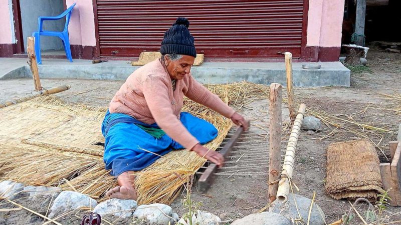 लमजुङ राइनास नगरपालिका–३ टिमुरेका ७५ वर्षीय हरिमाया अधिकारी  गुन्द्री बुन्ने क्रममा । आधुनिक प्रविधिको सामग्री आएपनि धानको परालबाट गुन्द्री बुन्ने र यसको प्रयोग अझै बढ्दो छ । तस्विरः जनक श्रेष्ठ/ रासस