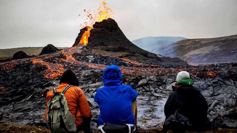 TOPSHOT - Sunday hikers look at the lava flowing from the erupting Fagradalsfjall volcano some 40 km west of the Icelandic capital Reykjavik, on March 21, 2021. - Weekend hikers took the opportunity Sunday to inspect the area where a volcano erupted in Iceland on March 19, some 40 kilometres (25 miles) from the capital Reykjavik, the Icelandic Meteorological Office said, as a red cloud lit up the night sky and a no-fly zone was established in the area. (Photo by Jeremie RICHARD / AFP)