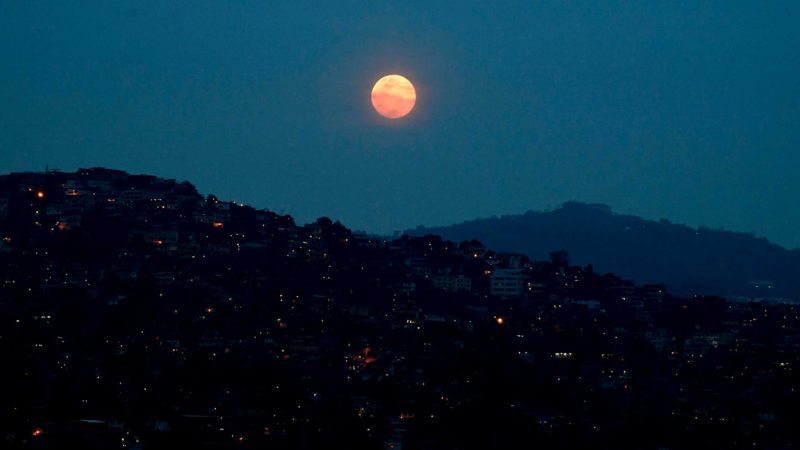 The full "Super Pink Moon" is seen over the Petare neighborhood in Caracas, on April 26, 2021. (Photo by Federico Parra / AFP)