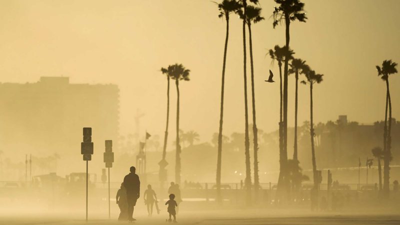 People walk and skateboard on a beach path as evening winds kick up sand Sunday, April 18, 2021, in Long Beach, Calif. (AP Photo/Ashley Landis)