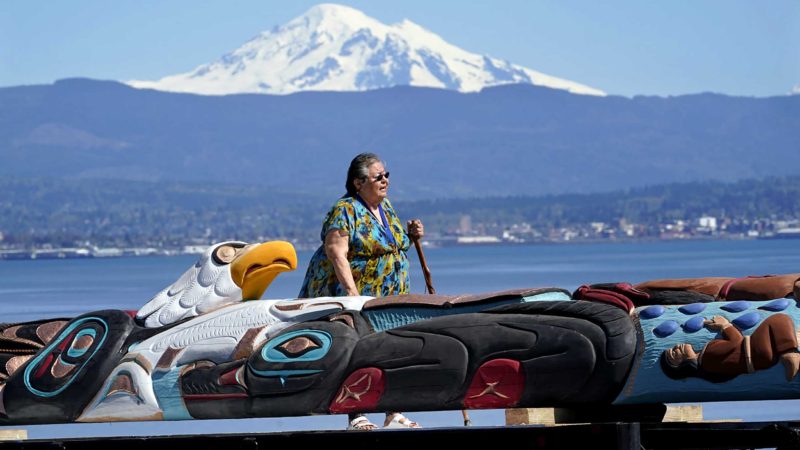 Lummi Nation elder Lucille Spencer prays over a nearly 25-foot totem pole, to be gifted from the tribe to the administration of President Joe Biden, in view of Mount Baker, behind, shortly after the pole was moved from a carving shed Monday, April 19, 2021, on the Lummi Reservation, near Bellingham, Wash. The pole, carved from a 400-year old red cedar, will make a journey from the reservation past sacred indigenous sites, before arriving in Washington, D.C., in early June. Organizers said that the totem pole is a reminder to leaders to honor the rights of Indigenous people and their sacred sites. (AP Photo/Elaine Thompson)