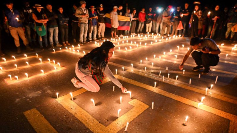 People gather around candles and words on the pavement reading "Minga resists" during a vigil for a woman who was raped during protests against the government, in Caldono, Colombia on May 14, 2021. - A 17-year-old girl committed suicide after being dragged and allegedly groped by police who were dissolving a protest in Colombia, denounced an independent human rights network, unleashing new demonstrations against the public force. (Photo by Luis ROBAYO / AFP)