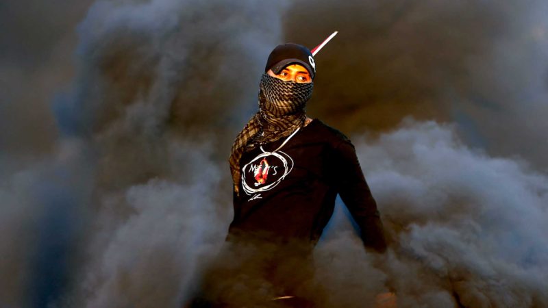 TOPSHOT - A Palestinian demonstrator stands amidst smoke from burn tires during a protest against the tension in Jerusalem and the Israeli-Gaza fighting, on May 17, 2021 in the occupied West Bank, near the settlement of Beit El next to Ramallah. (Photo by ABBAS MOMANI / AFP)