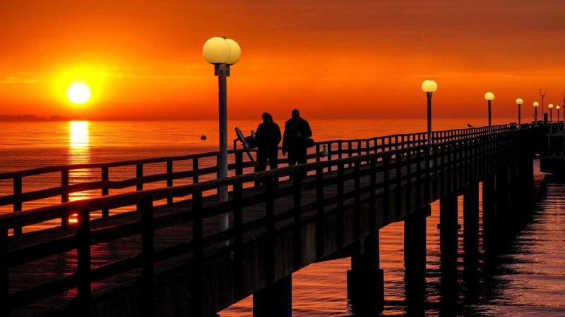 People walk on the pier at the Baltic Sea in Scharbeutz, Germany, as the sun rises Monday, June 7, 2021. (AP Photo/Michael Probst)