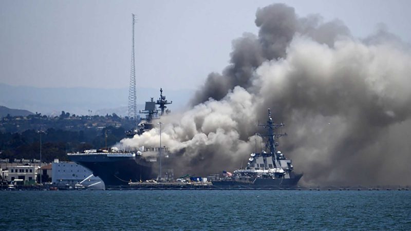 FILE - In this July 12, 2020, file photo, smoke rises from the USS Bonhomme Richard at Naval Base San Diego in San Diego after an explosion and fire. The U.S. Navy said Thursday, July 29, 2021, that charges have been filed against a sailor who is accused of starting a fire last year that destroyed a warship docked off San Diego. The amphibious assault ship called the USS Bonhomme Richard burned for more than four days and was the Navy's worst U.S. warship fire outside of combat in recent memory. (AP Photo/Denis Poroy, File)