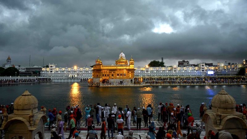 Sikh devotees wait for their turn to pay respect at the Golden Temple during a rainfall in Amritsar on July 11, 2021. (Photo by NARINDER NANU / AFP)