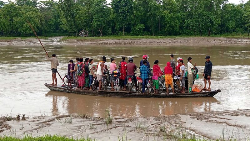 कैलालीको भजनी नगरपालिकामा पर्ने कान्द्रा नदी डुङ्गामार्फत वारपार गर्दै स्थानीय बासिन्दा । हुलाकी राजमार्गमा निर्माण हुन लागेको पुल दस वर्षसम्म पनि निर्माण सम्पन्न नभएपछि वर्षातको समयमा स्थानीय बासिन्दा ज्यानको जोखिम मोलेर डुङ्गाबाट नदी वारपार गर्दै आएका छन् । तस्वीर : झलनाथ खनाल/रासस
 