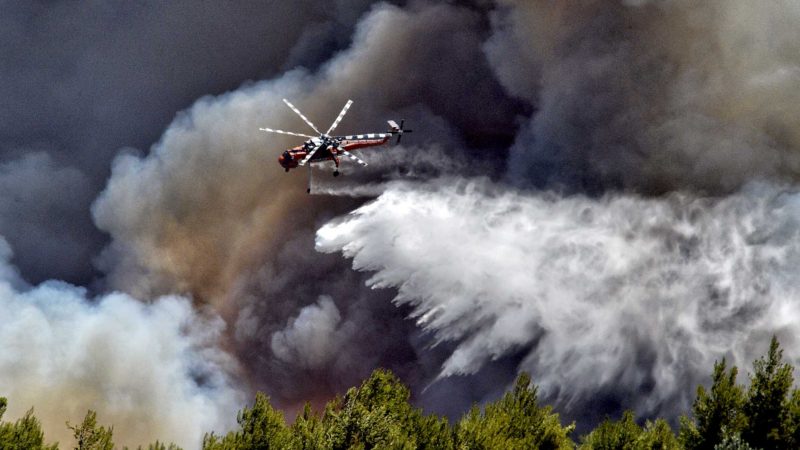 A firefighting helicopter drops water over a forest fire at Spathovouni village, near Corinth, southwest of Athens, Friday, July 23, 2021. Fire brigade vehicles are assisted by two helicopters and four firefighting planes in an effort to extinguish the fire. (AP Photo/Valerie Gache)