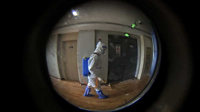 Seen through a door peephole, a medical worker wearing a protective clothing disinfects the corridor of a hotel used for foreigners to stay during a period of health quarantine in Shanghai, China, Thursday, Aug. 12, 2021. More than 30 Chinese officials have been fired or received other punishments over accusations they failed to respond properly to the latest surge of the coronavirus in the country. (AP Photo/Andy Wong)