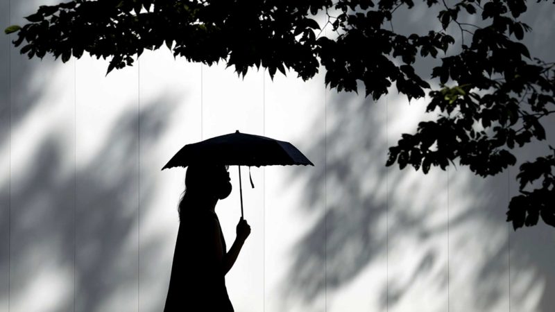 A woman wearing a face mask to help protect against the spread of the coronavirus walks under the scorching sun Wednesday, Aug. 11, 2021, in Tokyo, Japan. (AP Photo/Eugene Hoshiko)