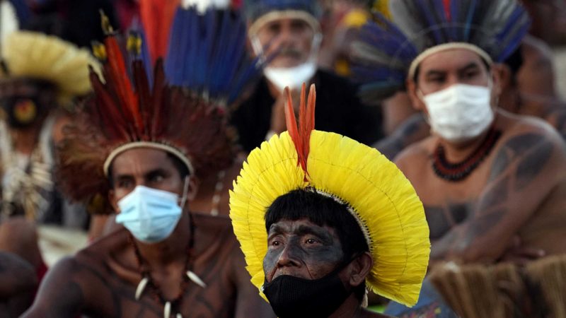 Indigenous people watch a Supreme Court session on a TV screen, that is expected to issue a ruling that will have far-reaching implications for tribal land rights, outside the Supreme Court building, in Brasilia, Brazil, Wednesday, Aug. 25, 2021. (AP Photo/Eraldo Peres)