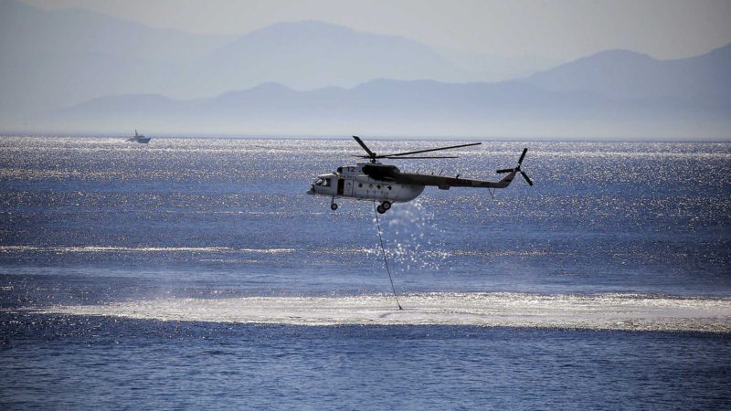 A helicopter takes water from the sea to extinguish a fire in Cokertme village, in Bodrum, Mugla, Turkey, Monday, Aug. 2, 2021. For the sixth straight day, Turkish firefighters were battling Monday to control the blazes tearing through forests near Turkey's beach destinations. Fed by strong winds and scorching temperatures, the fires that began Wednesday have left eight people dead and forced residents and tourists to flee vacation resorts in a flotilla of small boats.(AP Photo/Emre Tazegul)