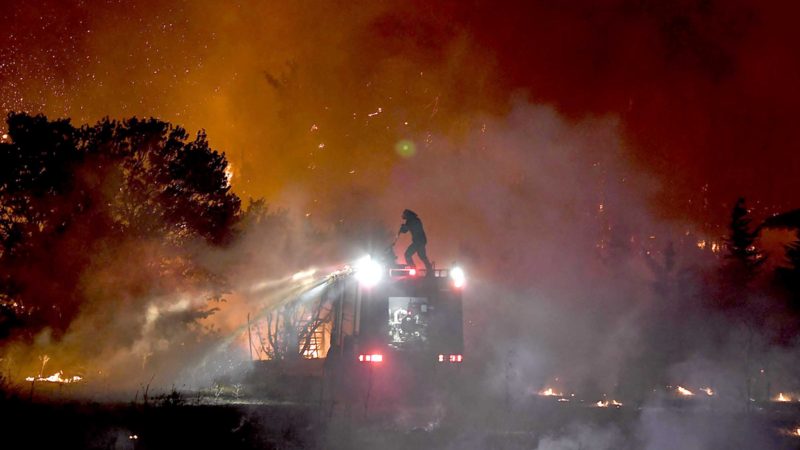 A fire fighter douse flames from the top of a truck as a fire spreads around the village of Afidnes, some 30 kilometres north of Athens on August 5, 2021. - Firefighters were battling a series of raging blazes in sweltering heat on August 5, 2021, in western and eastern Greece, and near Athens where a fire that had been coming under control regained strength. (Photo by LOUISA GOULIAMAKI / AFP)