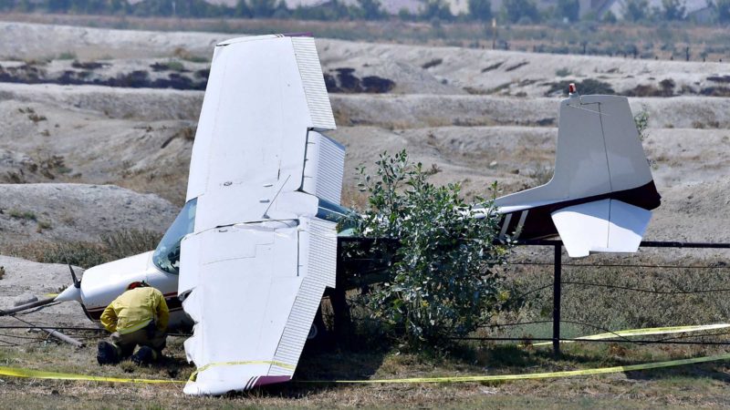 An Ontario firefighter checks under the fuselage of a crashed single-engine Cessna after a pilot made a forced landing due to engine trouble in a field south of Ontario Ranch Road in Ontario, Calif., Wednesday, Aug. 25, 2021. Authorities say a pilot escaped with minor injuries after a small plane made an emergency landing in a Southern California field on Wednesday. TV news footage from the scene showed the single-engine Cessna with its left wing in the grass near a main road in Ontario, about 40 miles east of downtown Los Angeles. (Will Lester/The Orange County Register via AP)